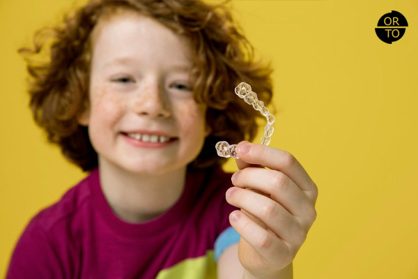 şeffaf plak (Invisalign First) tutan mutlu bir çocuk