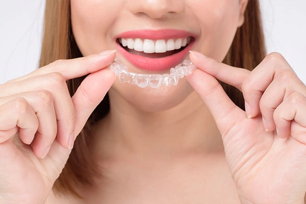 Genç bir kadın, dişlerine takmak üzere şeffaf ortodontik plak (aligner) tutuyor