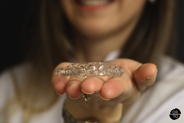 Bir kadın, avucunun içinde şeffaf ortodontik plak (Invisalign) tutuyor ve hafifçe gülümsüyor