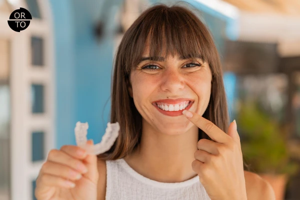 Elinde Invisalign şeffaf plak tutan mutlu yetişkin bir kadın