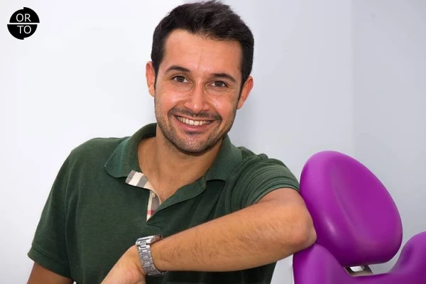 Gülümseyen ortodontist, ortodonti koltuğu yanında yeşil tişörtle poz veriyor.
